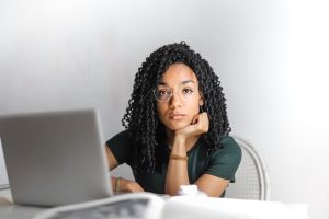 Young woman with glasses working attentively on a laptop at a bright desk.