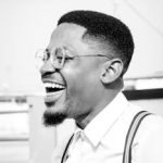 Black and white portrait of a joyful man in Accra, Ghana wearing stylish attire and glasses.